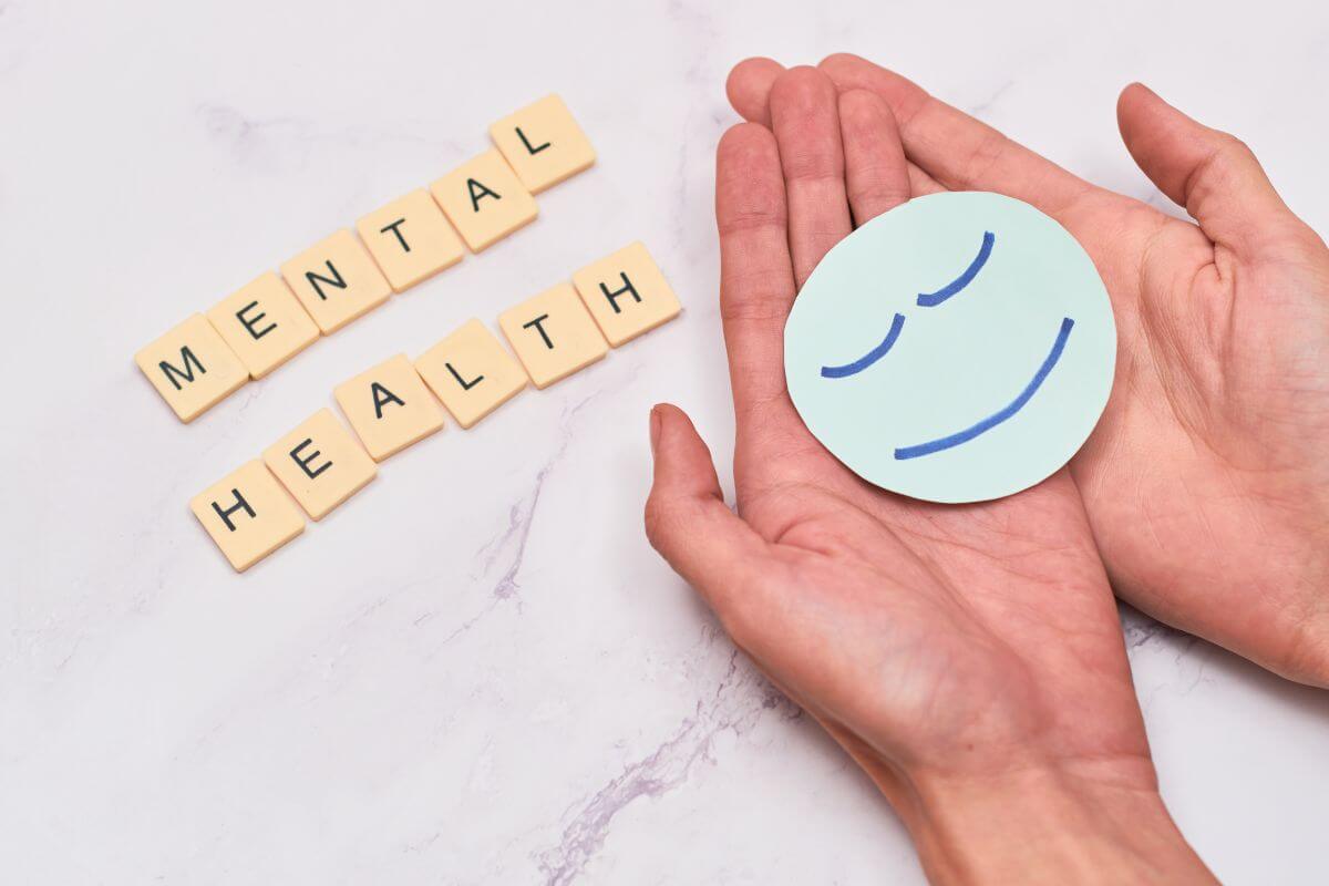 blocks with letters forming the word MENTAL HEALTH and a hand with a paper cut smiley